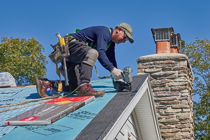 Roofer nailing GAF starter strip shingle over StormGuard leak barrier.