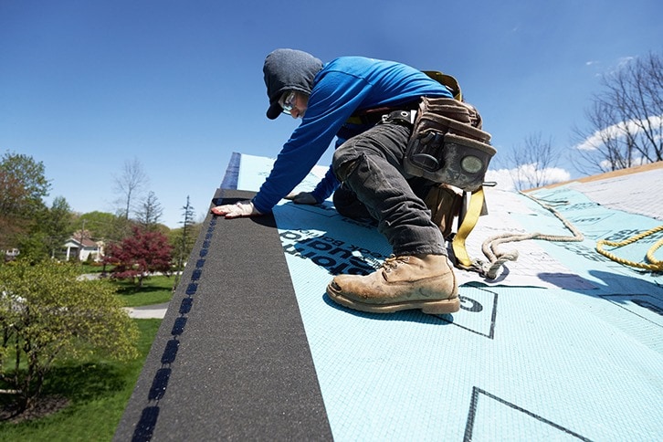 Roofer laying black starter strip shingle over blue GAF underlayment.