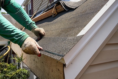 Roofer trimming and positioning first starter strip shingle at roof eave.