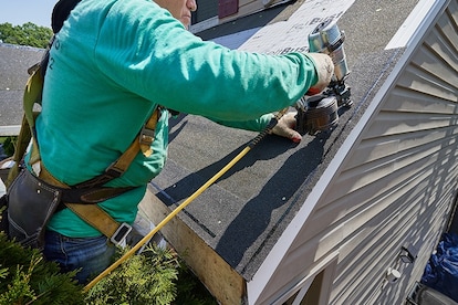 Installing starter strip shingles along roof rake edge with nail gun.