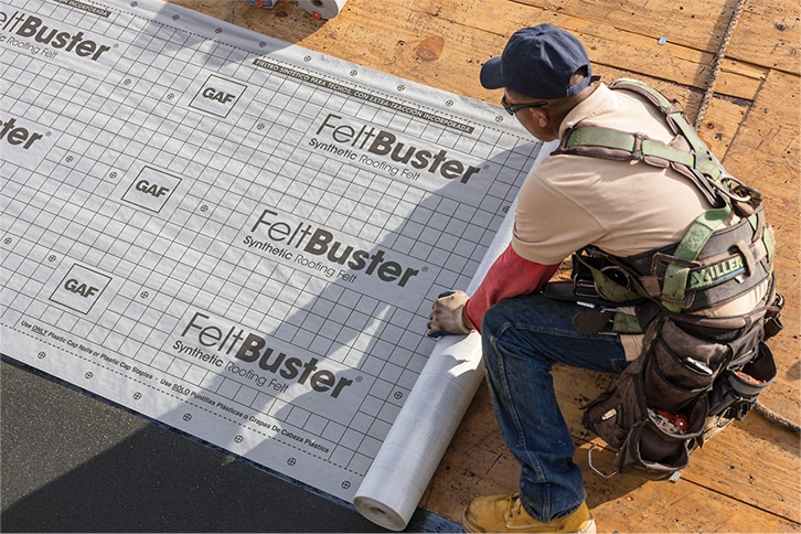 Contractors installing GAF synthetic roofing underlayment on a roof.
